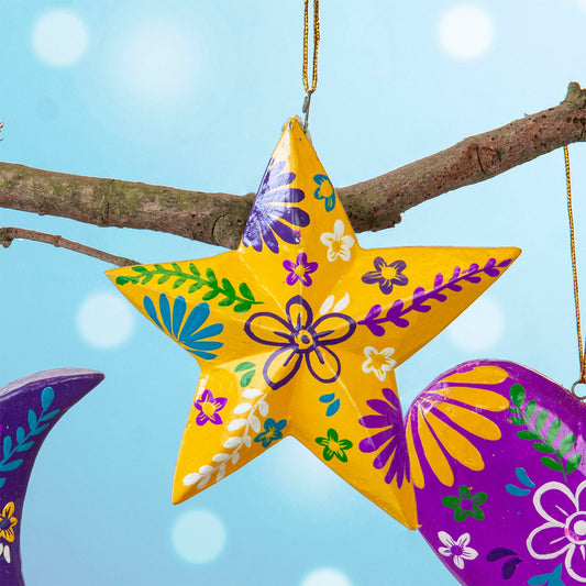 Yellow hand-painted wood star hanging with purple and blue floral motifs, Bali Indonesia, on branch with other decorations