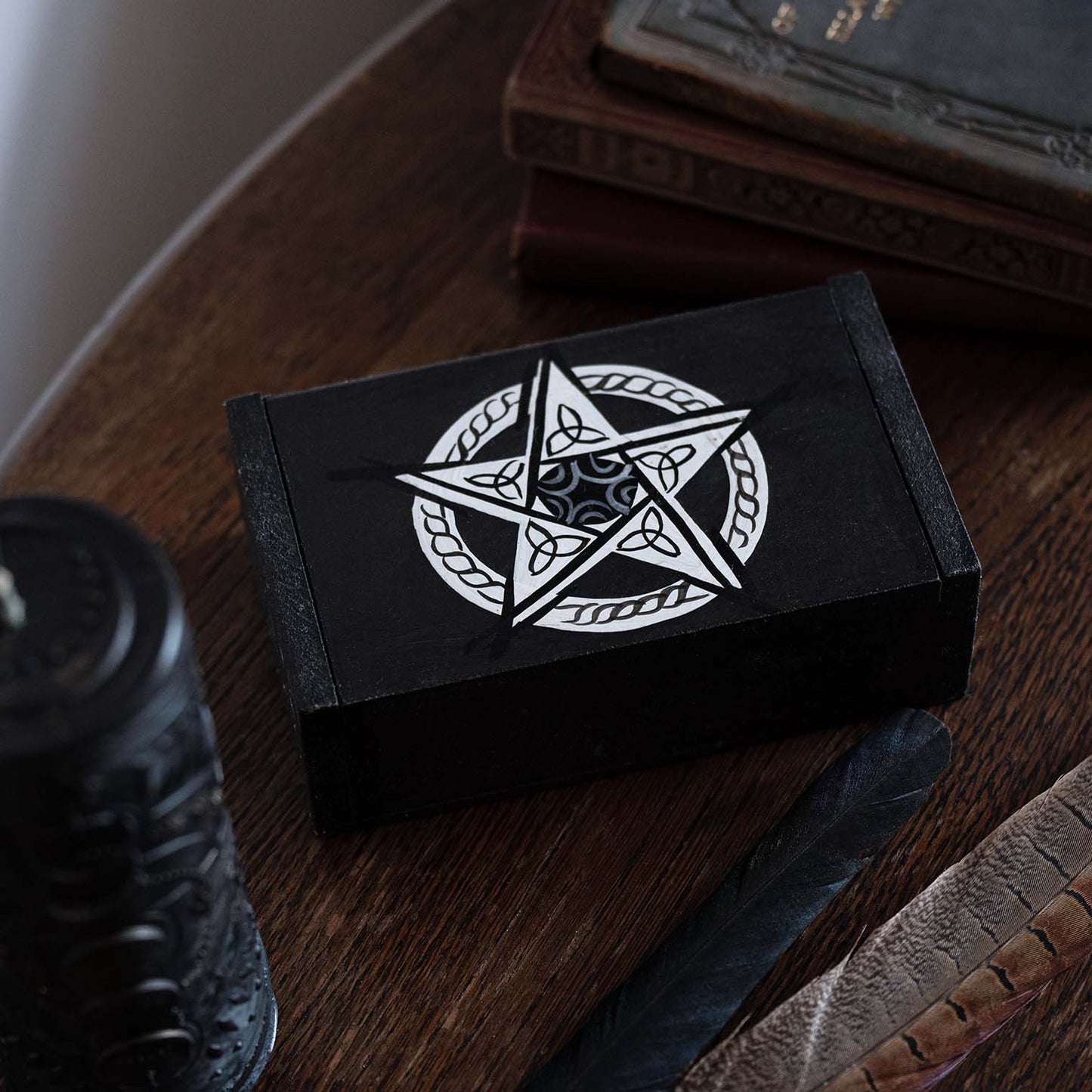 Black wooden pentacle box on a dark wood desk with candle and feathers, showing silver knotwork star on lid, Bali