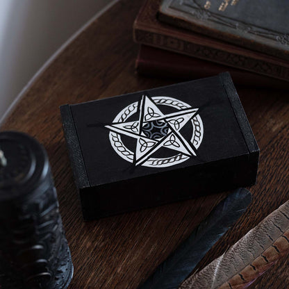 Black wooden pentacle box on a dark wood desk with candle and feathers, showing silver knotwork star on lid, Bali