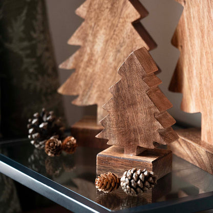 Hand-carved mango wood Christmas tree with stepped silhouette on square base, displayed with pinecones and seasonal décor