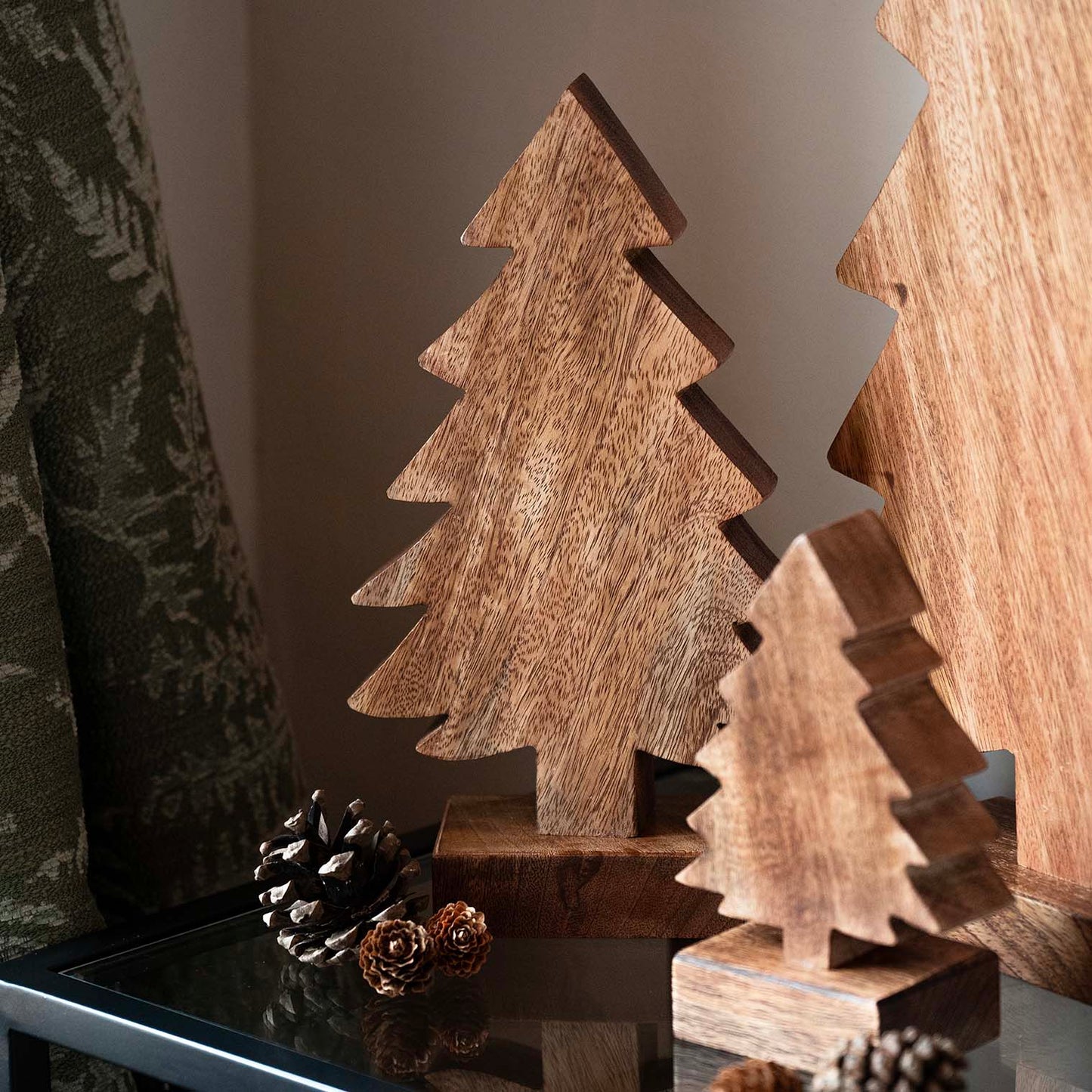 Hand-carved mango wood Christmas tree with stepped silhouette and dark finish, displayed with pinecones and evergreen accents