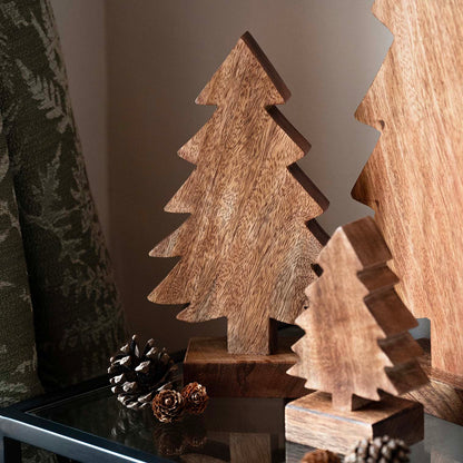 Hand-carved mango wood Christmas tree with stepped silhouette and dark finish, displayed with pinecones and evergreen accents