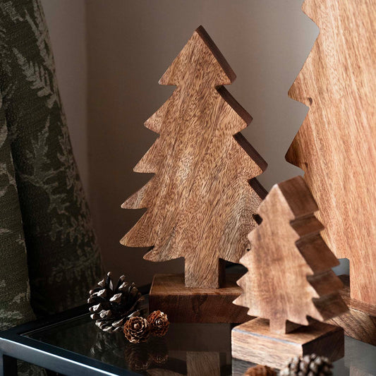 Hand-carved mango wood Christmas tree with stepped silhouette and dark finish, displayed with pinecones and evergreen accents