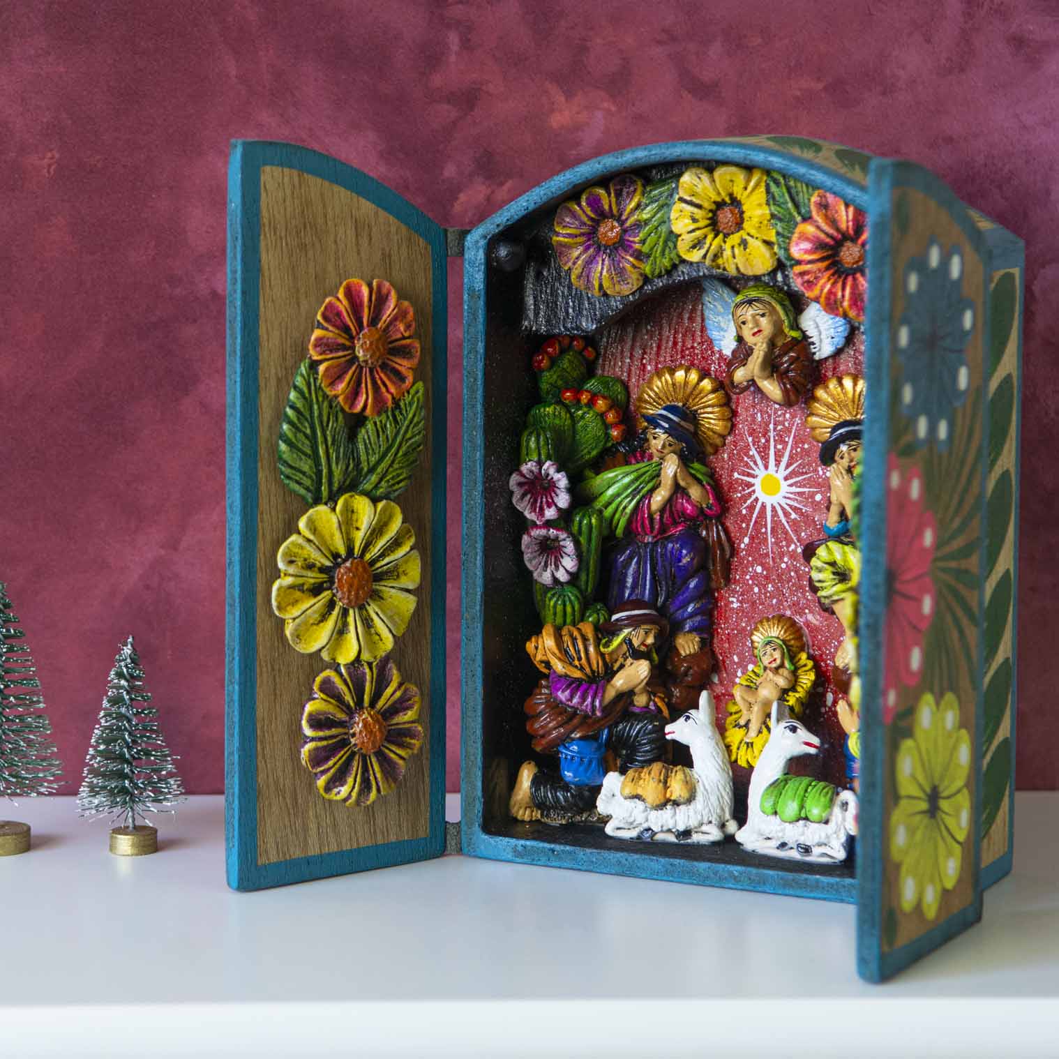 Peruvian nativity retablo open at an angle, showing painted clay figures inside and carved flowers on left door panel