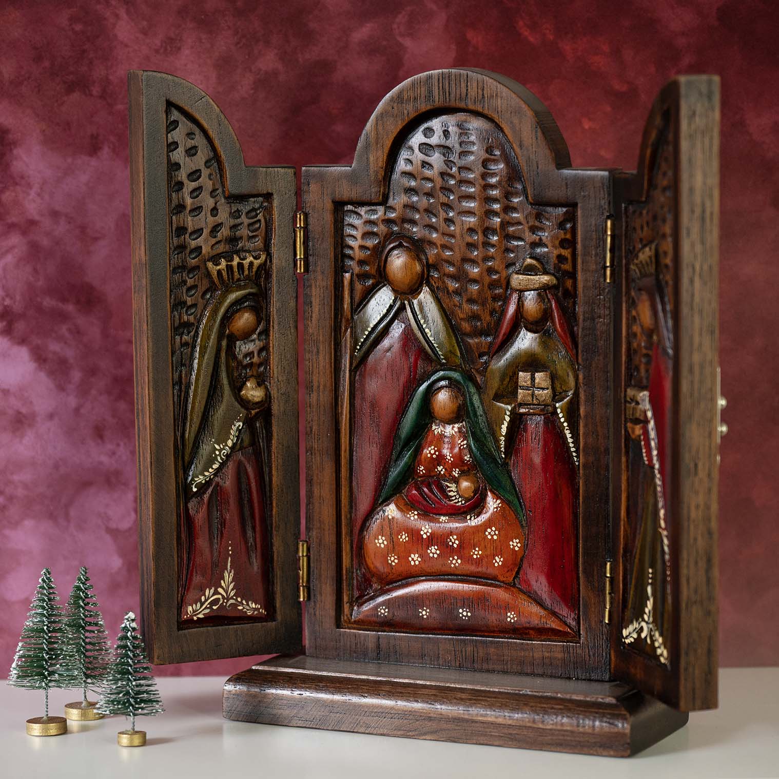 Cedar wood nativity triptych open at an angle, showing carved relief nativity scene in red and green, Peru, festive setting