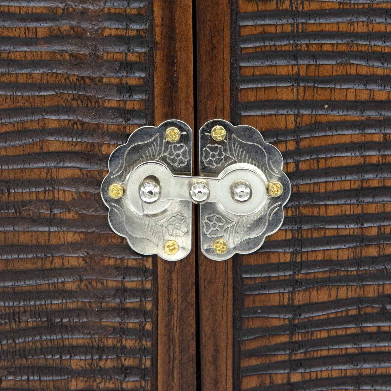 Close-up of metal clasp on cedar triptych doors, showing engraved floral detail against chisel-textured wood