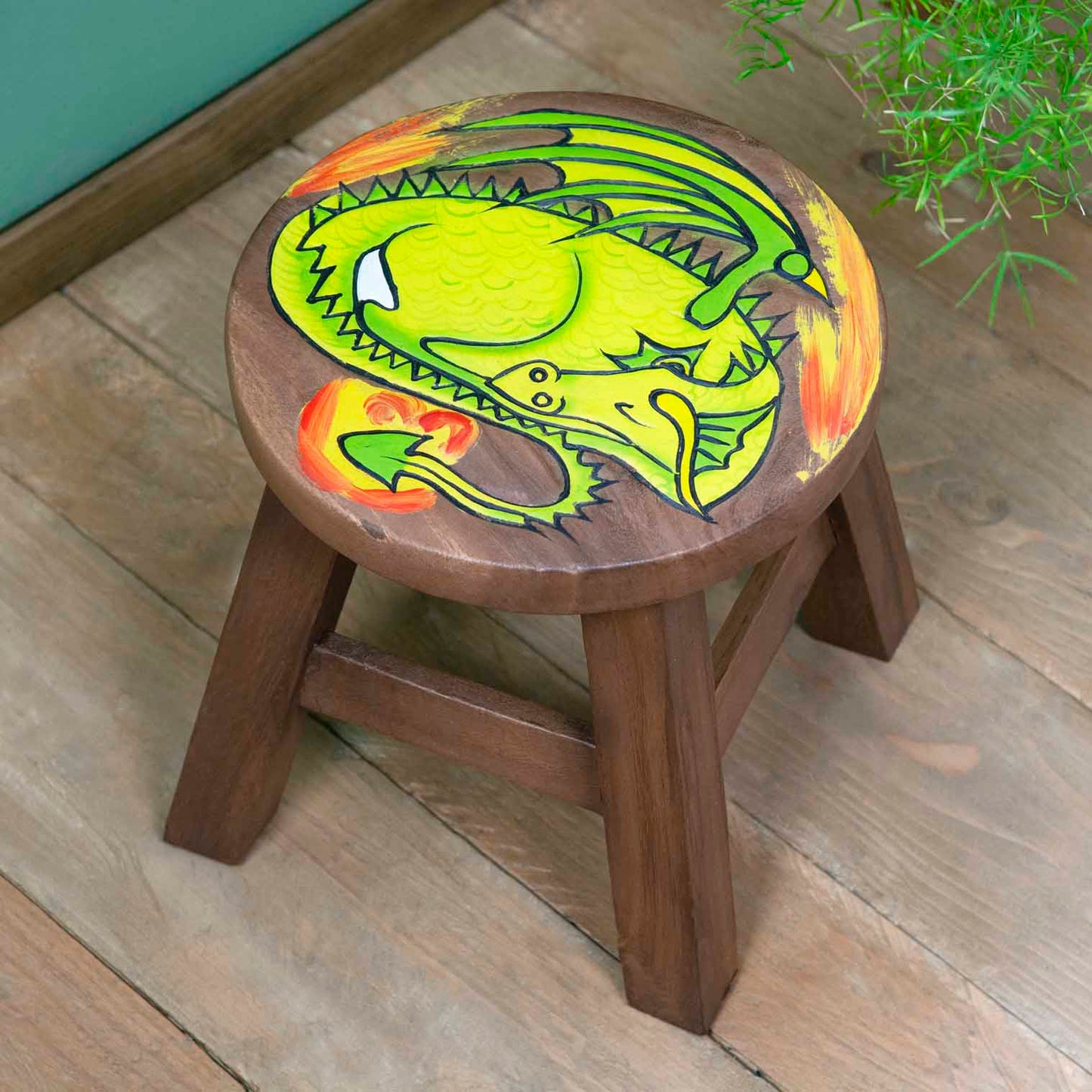 Raintree wood sleeping dragon stool with carved green dragon and orange flame, angled view on wooden floor, northern Thailand