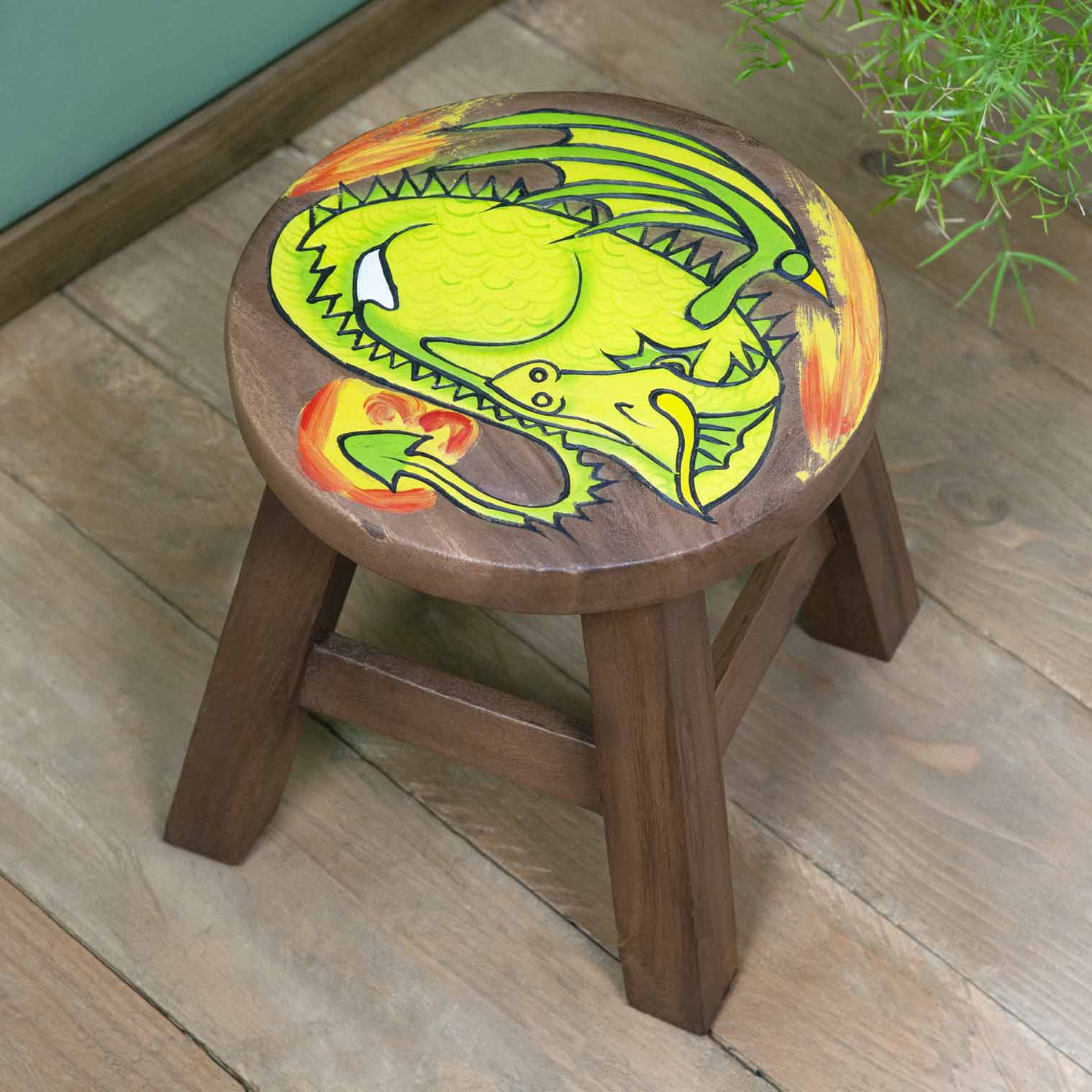 Raintree wood sleeping dragon stool with carved green dragon and orange flame, angled view on wooden floor, northern Thailand