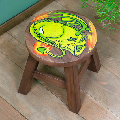 Raintree wood sleeping dragon stool with carved green dragon and orange flame, angled view on wooden floor, northern Thailand