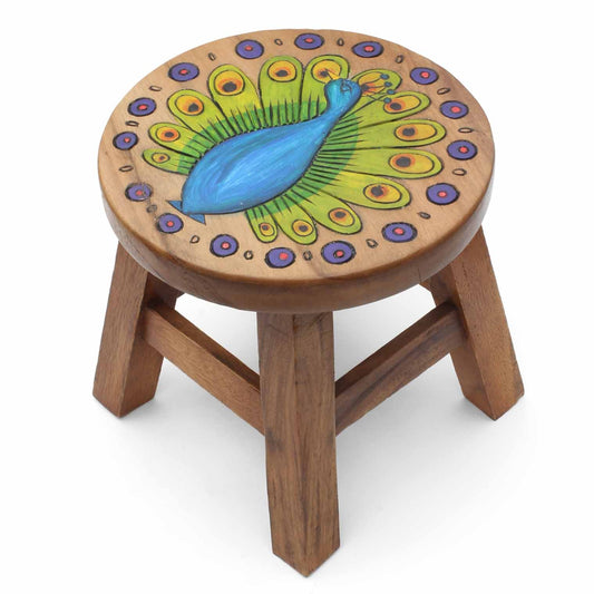 Hand-carved peacock stool in Raintree wood on white background, cobalt blue body with full tail display and painted feather e