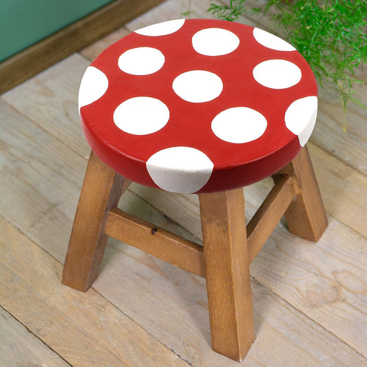 Raintree wood mushroom stool with red and white spotted seat resembling fly agaric cap, angled view on wooden floor, Thailand