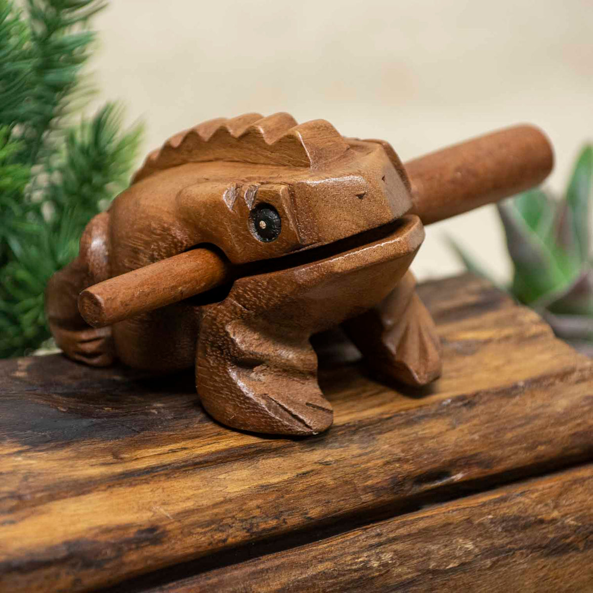 Rain Tree wood frog guiro with striker resting on wooden surface, front three-quarter view, northern Thailand