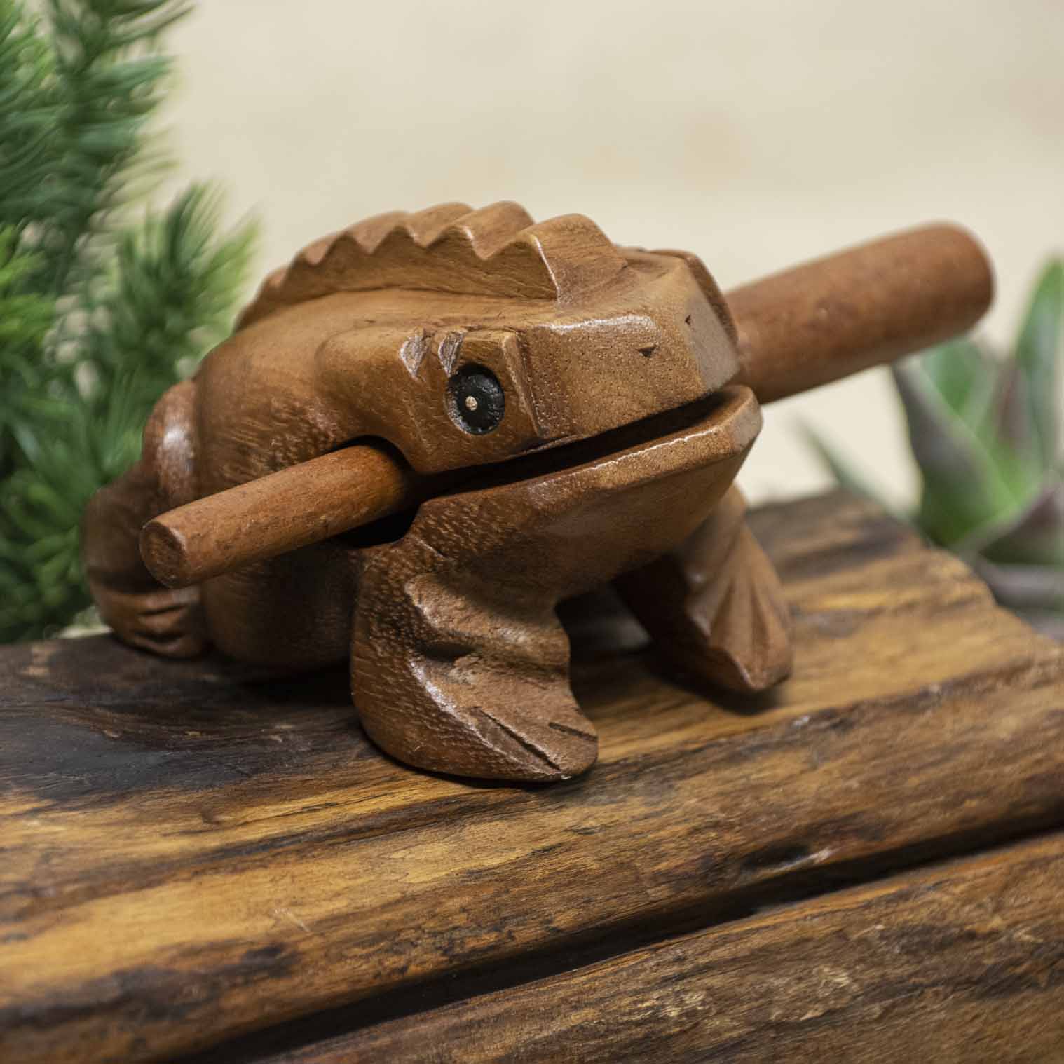 Rain Tree wood frog guiro with striker resting on wooden surface, front three-quarter view, northern Thailand