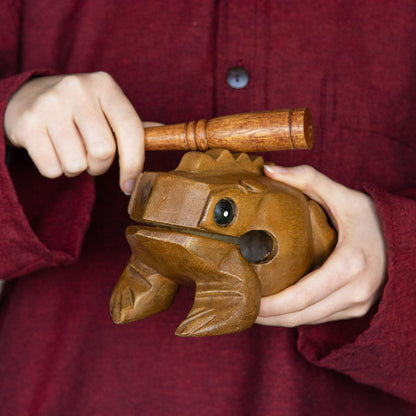 Hands holding medium acacia frog guiro and playing striker across ridged back, demonstrating playing position